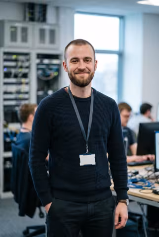 Early-career IT staff portrait, services office background — Person `person_portrait`.