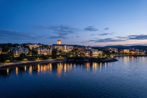 Campus at dusk, lights reflected over water — Landing page imagery, atmospheric hero.