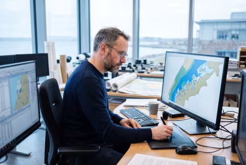 GIS specialist tracing a shoreline layer at a mapping workstation — Person `main_image`, staff/data.