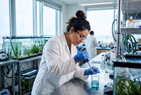 Graduate researcher at a wet lab bench with sample beaker — Person `main_image`, student/researcher.