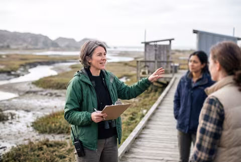 Marine policy researcher briefing colleagues at a field station overlook — Person `main_image`, faculty/staff.