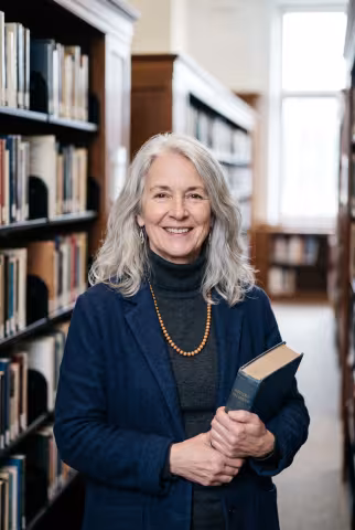 Senior faculty portrait, library stacks background — Person `person_portrait`.