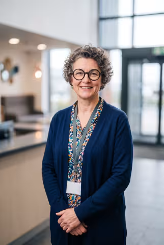 Student services adviser portrait, reception area background — Person `person_portrait`.